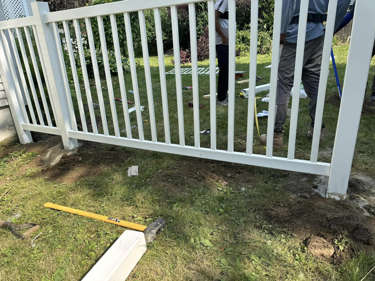 A close-up view of a newly installed white fence post set in the ground by T & A Fencing in Warren, MI, with tools nearby.
