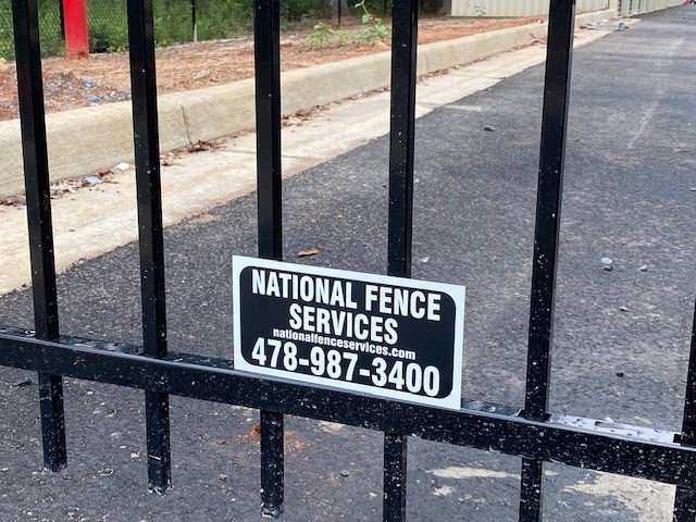 A close-up view of a black ornamental fence featuring the National Fence Services, LLC sign, installed in Macon, GA.