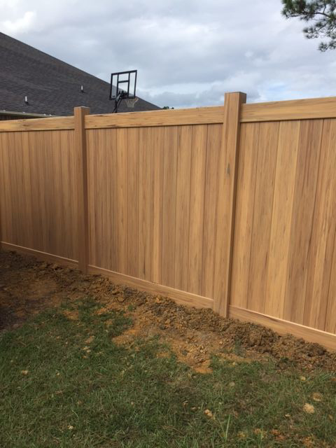 A close-up view of the base of a light brown privacy fence, showing the quality installation by Custom Fence Builders in Gulfport, MS.