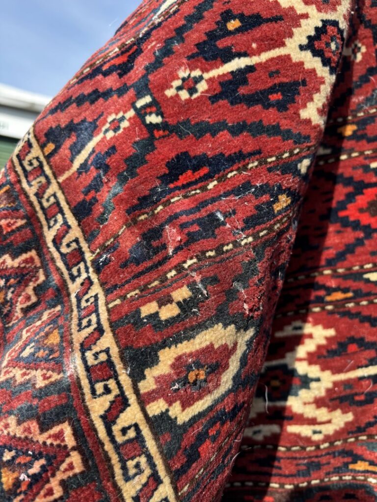 Close-up view of a red oriental rug, possibly undergoing inspection or cleaning by Duke Brothers Oriental Rug Cleaning in Norfolk, VA.