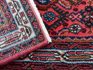 A close-up view of a red patterned rug with a corner folded, suggesting quality inspection or repair by Carpet Cleaner Staten Island in Staten Island, NY.