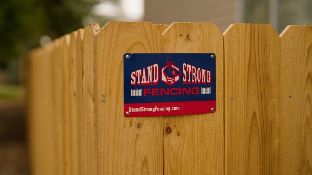 A close-up of a newly installed wood fence featuring the Stand Strong Fencing business sign in East Austin, TX.