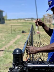 A close-up of a worker's hands attaching chain-link fence mesh to a top rail by Stallworth Home Improvement in Des Moines, IA.