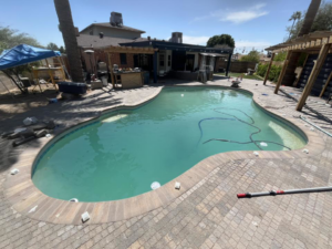 A swimming pool with cloudy water and cleaning equipment, showing a pool in need of service by Brigade Pool Services in Tempe, AZ.