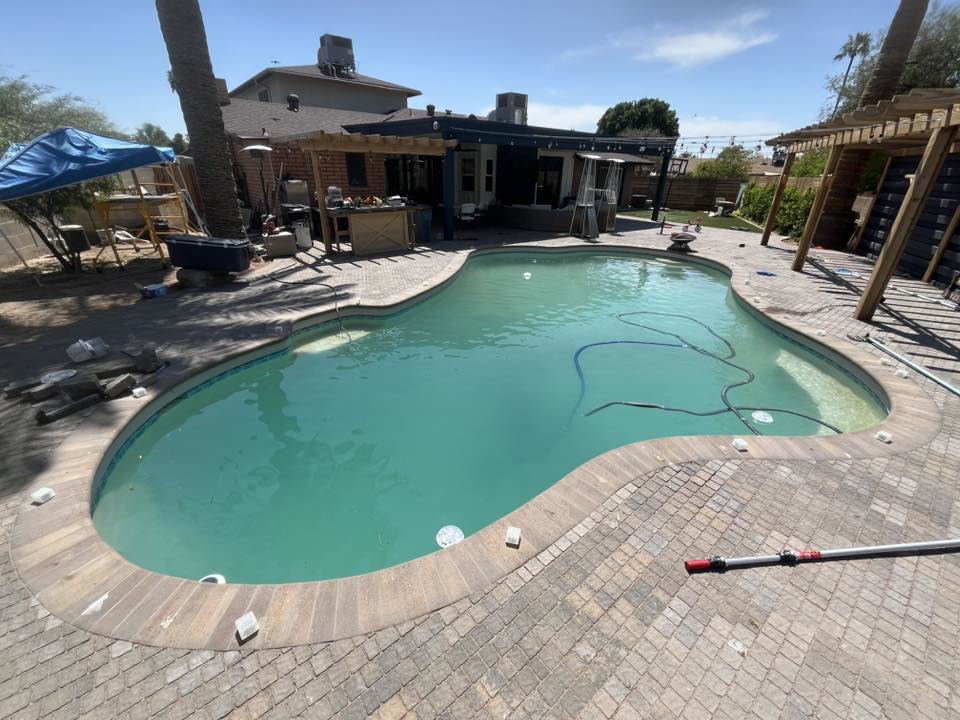 A swimming pool with cloudy water and cleaning equipment, showing a pool in need of service by Brigade Pool Services in Tempe, AZ.