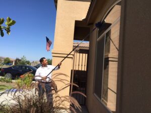 A Dan's Pest Management technician removing cobwebs from a house exterior in Bakersfield, CA