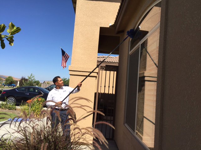 A Dan's Pest Management technician removing cobwebs from a house exterior in Bakersfield, CA