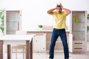 A man looking shocked at a severe cockroach infestation on the floor and furniture in a home, handled by Ares Pest Control in Biddeford, ME.