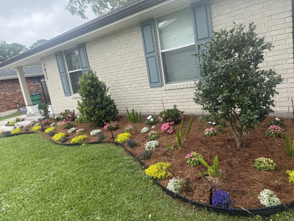 A vibrant, newly planted flower bed with various colorful flowers and fresh mulch in front of a house by God's Sight Lawn & Gardens LLC in New Orleans, LA
