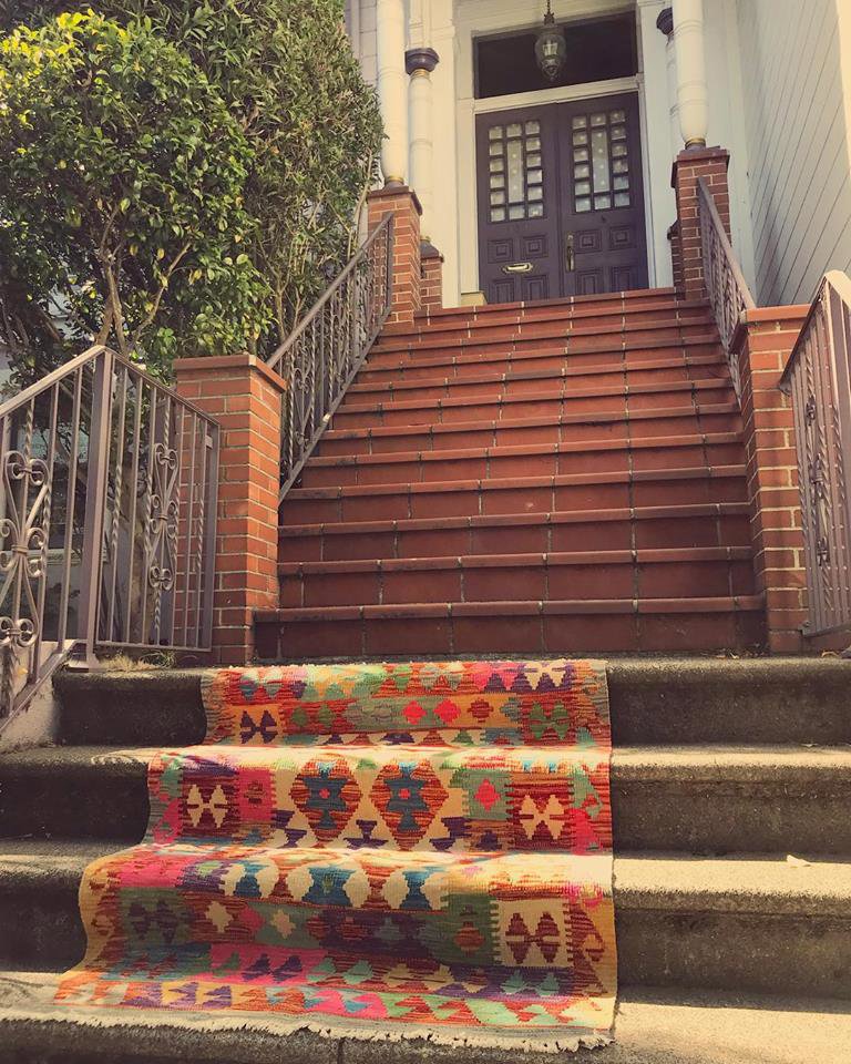 A vibrant patterned rug runner is laid out on outdoor brick steps by Nomad Rugs, a carpet contractor in San Francisco, CA.