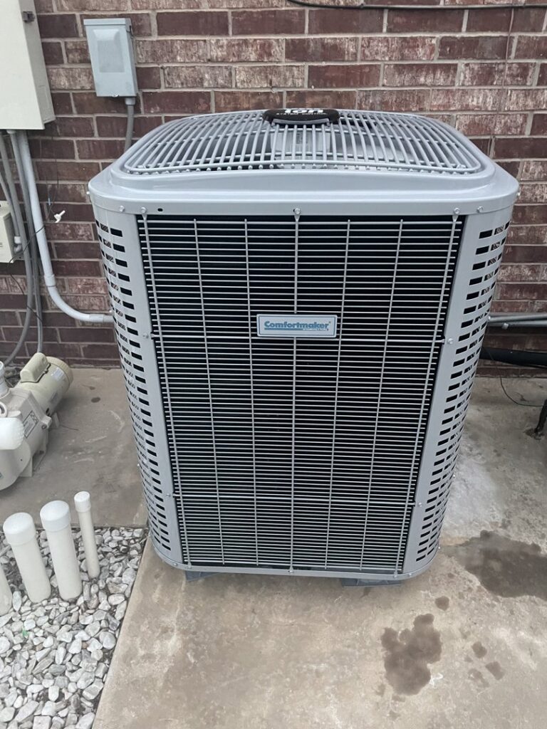 A Comfortmaker outdoor AC unit installed next to a brick wall, showcasing quality work by Rhino Heating and Air Conditioning LLC in Norman, OK.