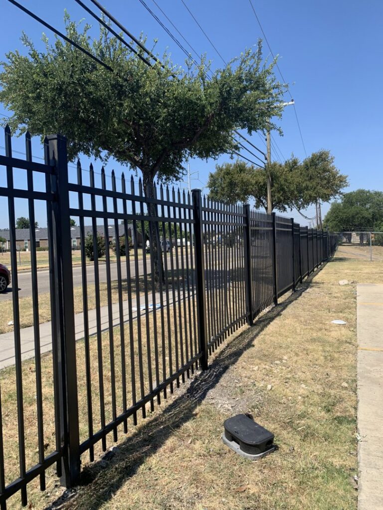 A long commercial black metal security fence with spiked tops installed by Craftsman Automatic Gates in Dallas, TX.