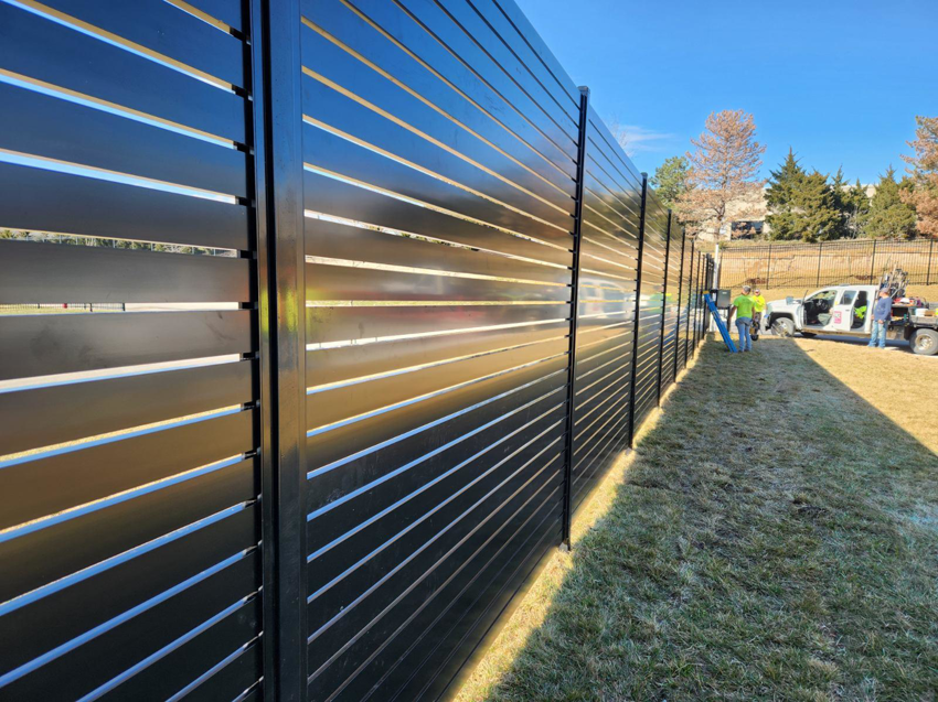 A long commercial black slatted fence being installed by Van's Fence in Kansas City, MO.