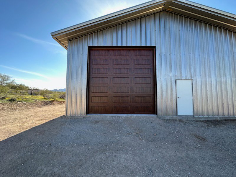 A large brown garage door installed on a metal commercial building by Johns Garage Doors in Tucson, AZ.