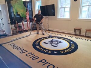 A technician cleaning a large commercial carpet with a logo at a business by Advanced Carpet Cleaning in College Station, TX