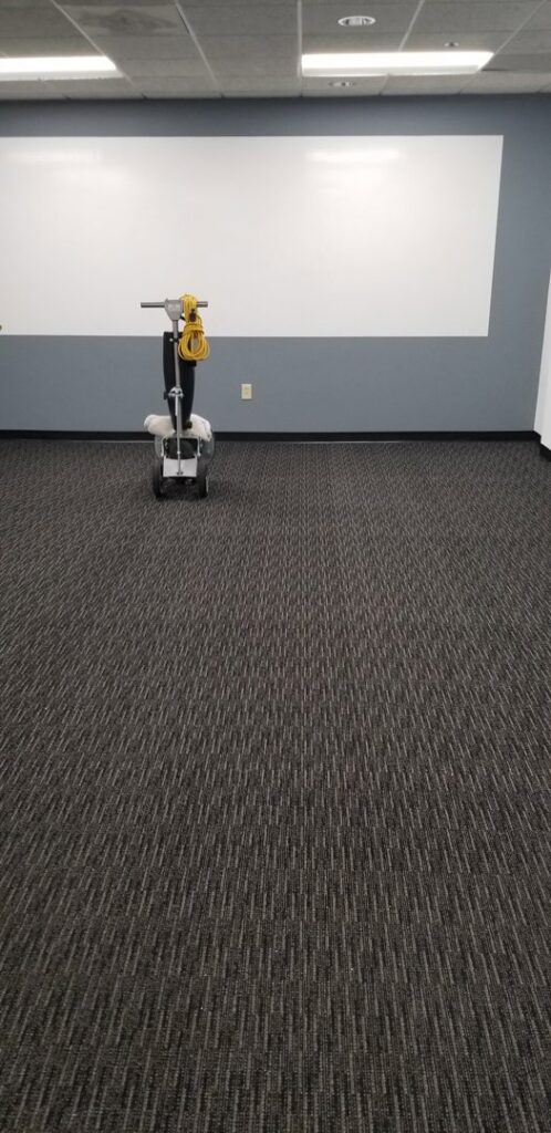 A commercial carpet cleaning machine positioned in an office space with dark patterned carpet by Steam Giant in Raleigh, NC.