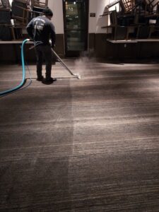 A professional cleaning a large commercial carpet in an event space with stacked chairs by Custom Carpet Cleaning in Albuquerque, NM.