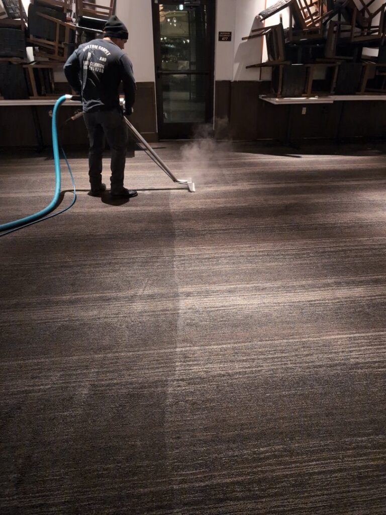 A professional cleaning a large commercial carpet in an event space with stacked chairs by Custom Carpet Cleaning in Albuquerque, NM.