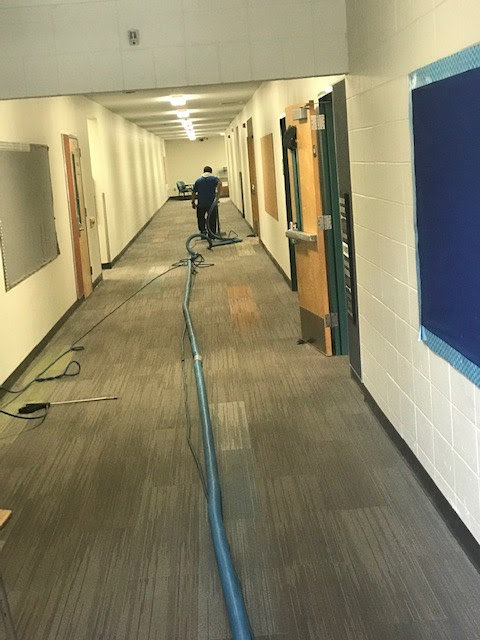 A worker performing commercial carpet cleaning in a long hallway for First Choice Janitorial Services in Vancouver, WA.