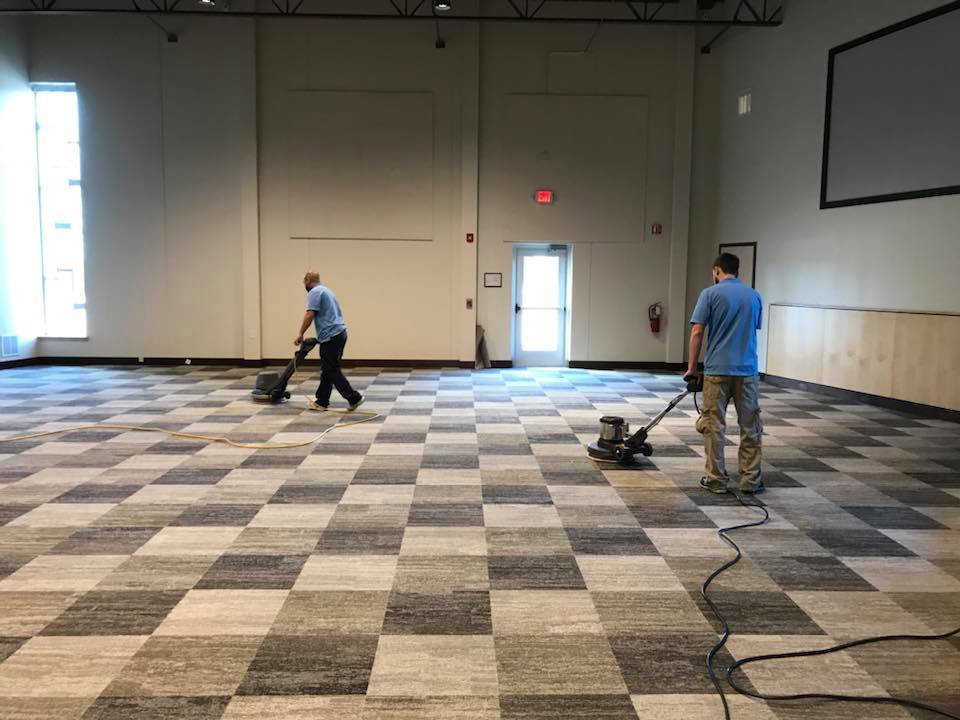 Two professionals performing commercial carpet cleaning on a checkered carpet in a large room for Heaven's Best Carpet Cleaning San Diego CA.