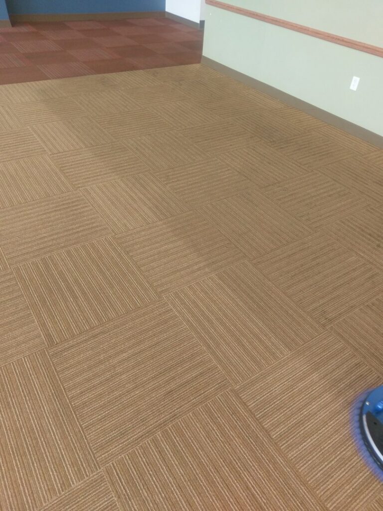 A commercial space with brown carpet tiles being professionally cleaned, showing a cleaning machine from Real Green Cleaning in Indianapolis, IN.
