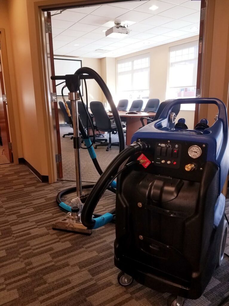 A professional carpet cleaning machine set up in an office hallway near a conference room by 765 Custom Cleaners in Lafayette, IN.