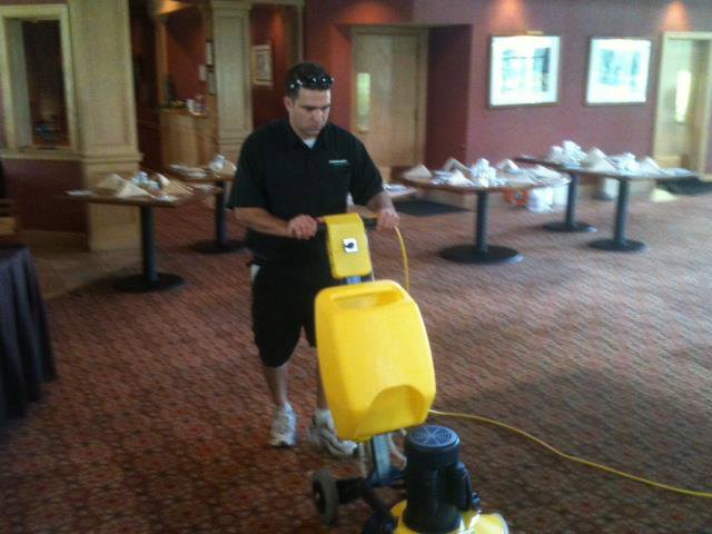 A technician operating a commercial rotary carpet cleaning machine on a patterned carpet for Steam Giant in Raleigh, NC.