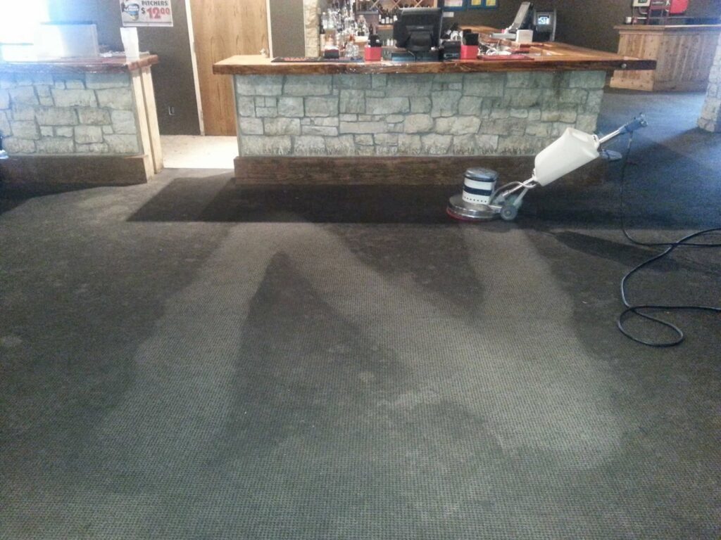 A commercial carpet cleaning machine in action on a dark carpet near a bar area by Royal Carpet & Upholstery Cleaning in Lincoln, NE.