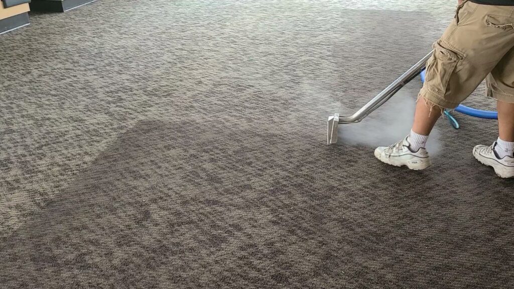 A professional cleaning a patterned commercial carpet with a wand, steam visible, by New Dawn's Carpet Cleaning in Cicero, IL.