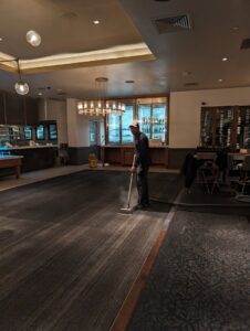 A professional cleaning a large commercial carpet in a restaurant or hotel lobby by Custom Carpet Cleaning in Albuquerque, NM.