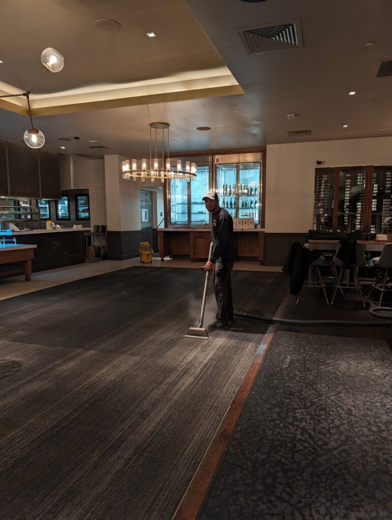 A professional cleaning a large commercial carpet in a restaurant or hotel lobby by Custom Carpet Cleaning in Albuquerque, NM.