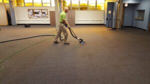 A professional performing commercial carpet cleaning on a large dark grey carpeted area for All Seasons Carpet Cleaning in Loves Park, IL.