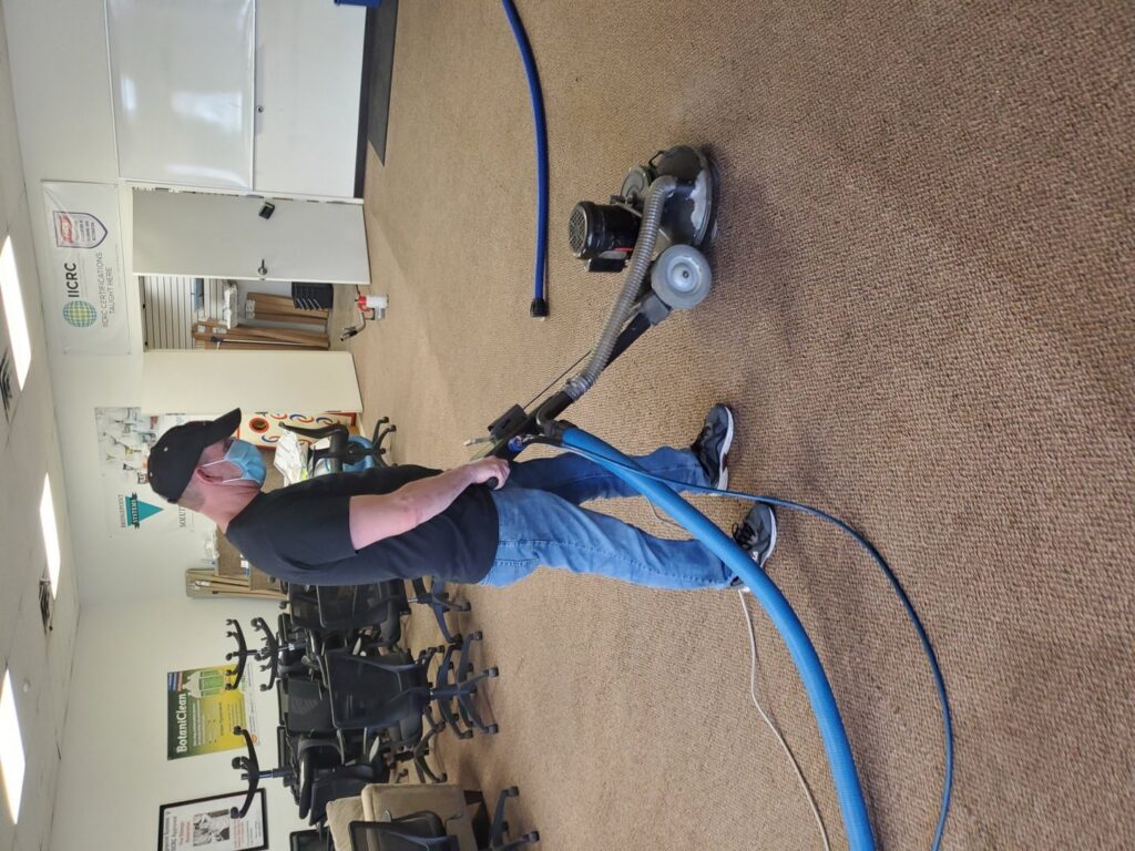 A masked technician operating a carpet cleaning machine in a commercial office space by STC Carpet Care in Arvada, CO