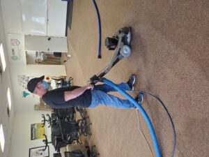 A masked technician operating a carpet cleaning machine in a commercial office space by STC Carpet Care in Arvada, CO
