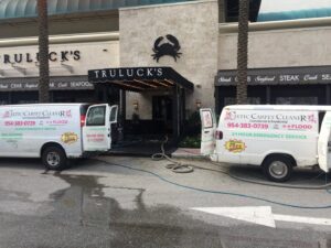 Celtic Carpet Cleaner vans with hoses outside Truluck's, indicating a commercial carpet cleaning job in Fort Lauderdale, FL.