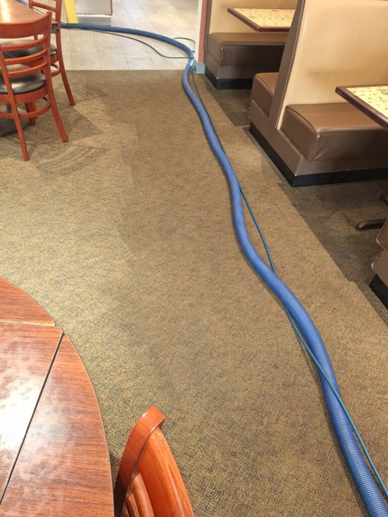 Commercial carpet cleaning in a restaurant with a cleaning wand and hose, showing a clean and dirty section, by Keith's Cleaning Service in Auburn, ME