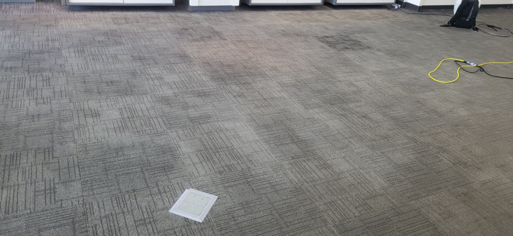 Commercial carpet tiles showing areas needing cleaning, with a power cord, by Leiter's Carpet Cleaning in Fort Wayne, IN.