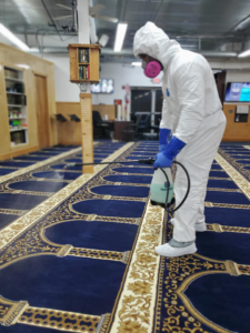 A technician in a hazmat suit performing commercial carpet disinfection on a large blue patterned carpet by Maxcarp Carpet Cleaning in Kent, WA.