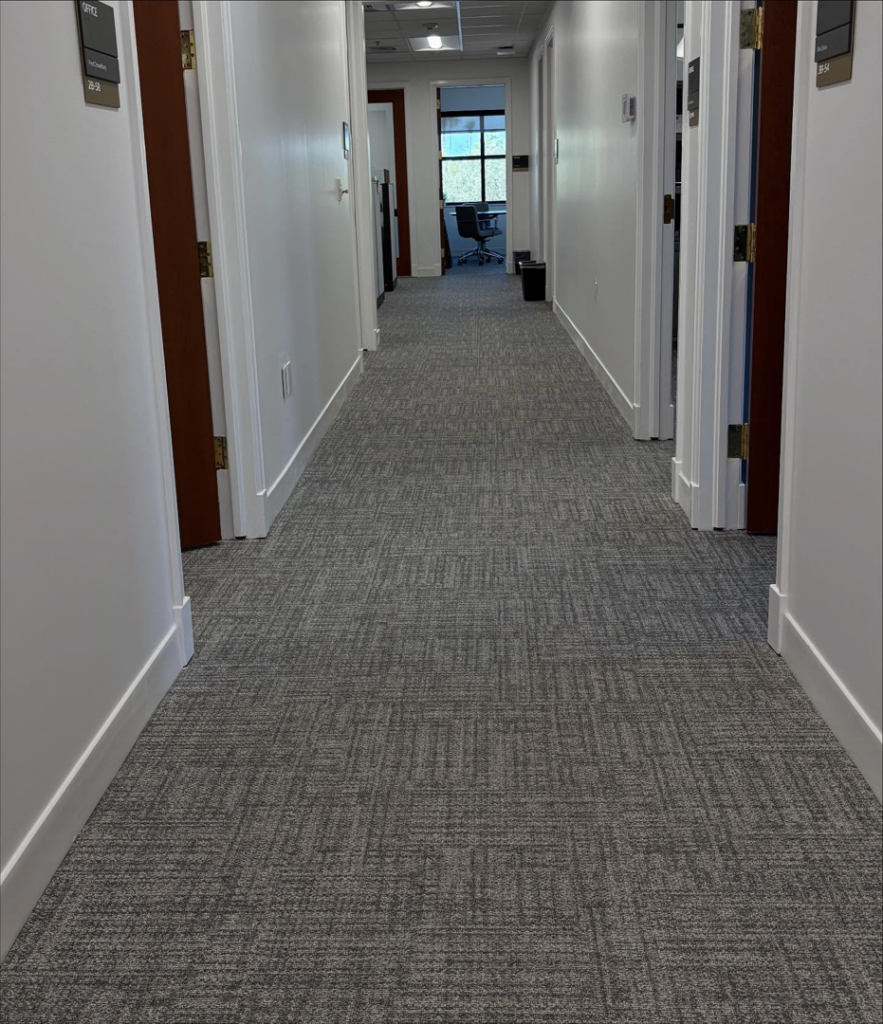 A long hallway in a commercial office building featuring newly installed grey patterned carpet by Rugs R Us Corporation in Fort Lauderdale, FL.