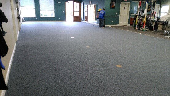A worker installing or cleaning commercial carpet in a large room by Plaza Carpets in Lexington, KY