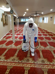 A technician in a hazmat suit performing commercial carpet sanitization on a large red patterned carpet by Maxcarp Carpet Cleaning in Kent, WA.