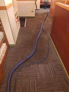 Commercial carpet tile cleaning in a hallway with a long blue hose, by Keith's Cleaning Service in Auburn, ME