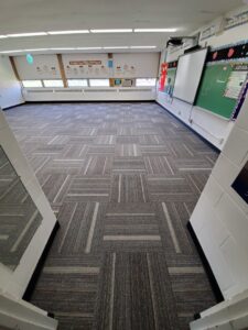 Professional installation of gray patterned carpet tiles in a large room by Integrated Flooring in Burton, MI.