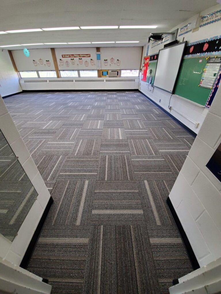 Professional installation of gray patterned carpet tiles in a large room by Integrated Flooring in Burton, MI.