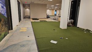A worker installing green turf-like commercial carpet in a large room for Carpets Direct Naperville, IL.