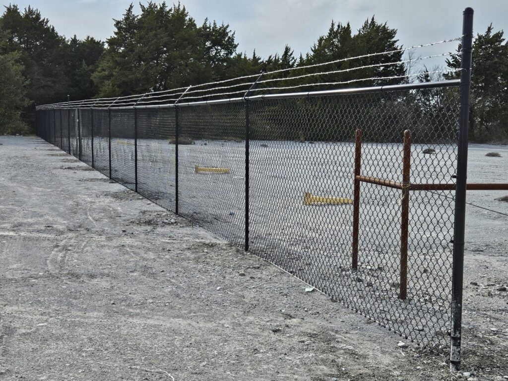 A long commercial chain-link fence topped with barbed wire, installed by QD & E Fencing in Fort Worth, TX.