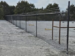 A long commercial chain-link fence topped with barbed wire, installed by QD & E Fencing in Fort Worth, TX.