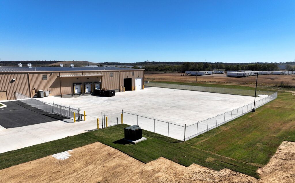 A commercial chain-link fence enclosing a large concrete area next to a building, installed by The Fence Man in Fort Smith, AR