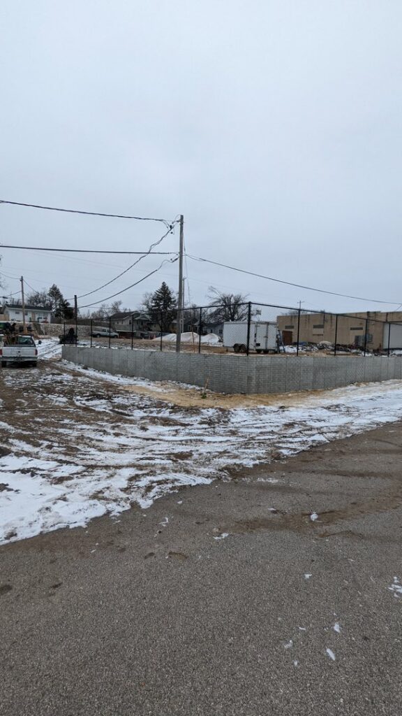 A chain-link fence installed alongside a concrete block retaining wall by Corridor Residential Fencing Co. in Cedar Rapids, IA.