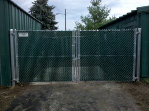 A commercial chain-link fence with green privacy slats and a double gate by Statewide Fencing, Inc. in Franksville, WI